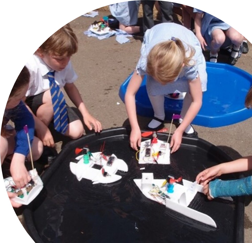 Children testing home-made electric boats in water trays in the school playground